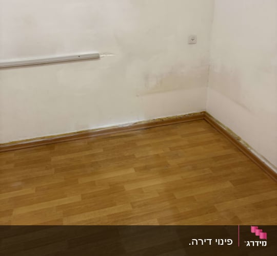 פינה של חדר עם רצפת עץ וקיר לבן